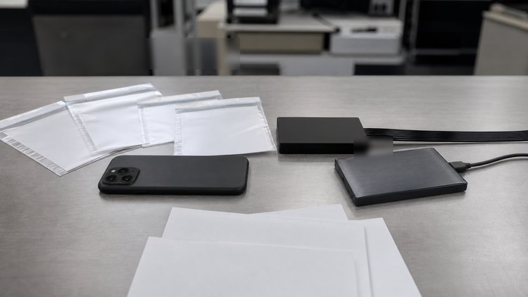 Closed phone, evidence sleeves, and external drives on a forensic workstation