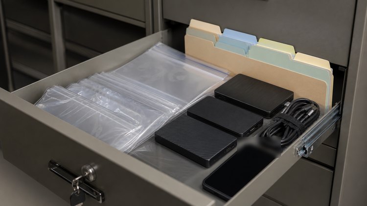 Evidence storage drawer with sealed bags, folders, drives, cables, and a powered-off phone